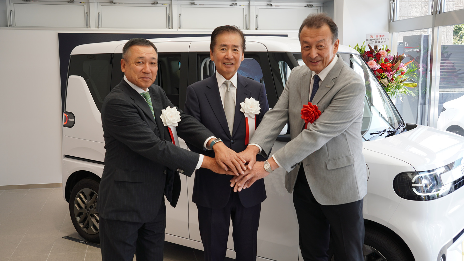 新型軽EV RACCOの前で手を重ねる3社の代表者